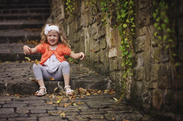 Roztomilé dítě dívka hraje a házení listy při posezení na staré kamenné cestě s schody — Stock fotografie