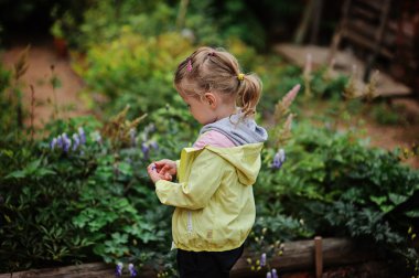 Yaz bahçesinde çiçekler ile oynarken hafif sarı ceketli çocuk kız