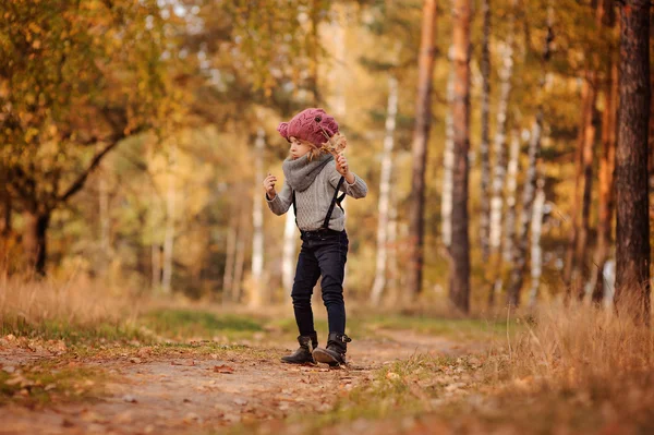 Menina adorável criança em chapéu de malha rosa e camisola cinza brincando com pau e folhas no passeio na floresta ensolarada outono — Fotografia de Stock