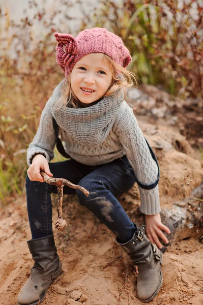 Söta barn flicka i rosa Stickad mössa vertikala porträtt på hösten flodsida med sandstrand — Stockfoto