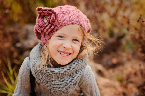 Close up horizontal portrait of adorable blonde blue eyed smiling child girl in pink knitted hat and grey sweater — Stock Photo, Image