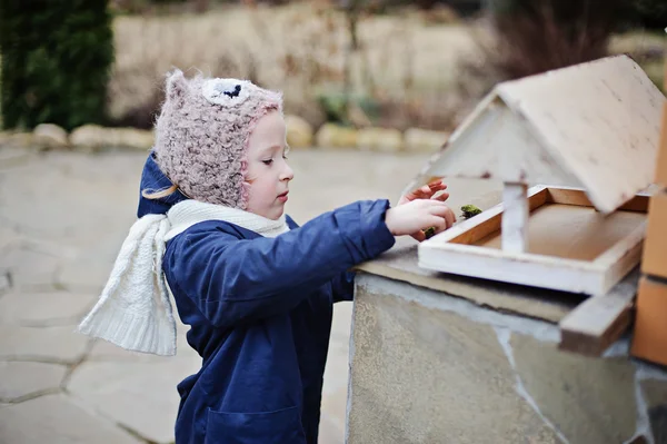 Cute child girl in blue coat plays with bird feeder in early spring garden — Stock Photo, Image