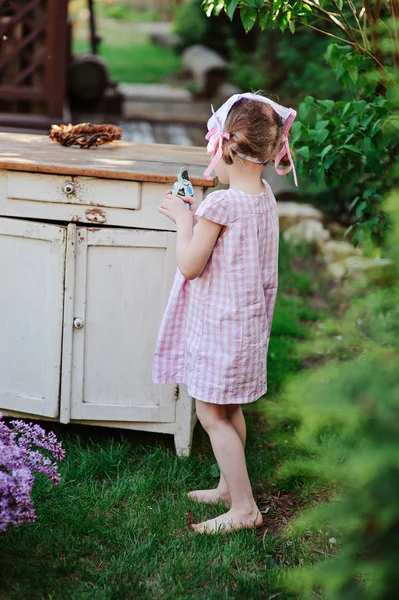 Child girl in pink plaid dress at wooden bureau with secateurs in spring garden — Stock Photo, Image