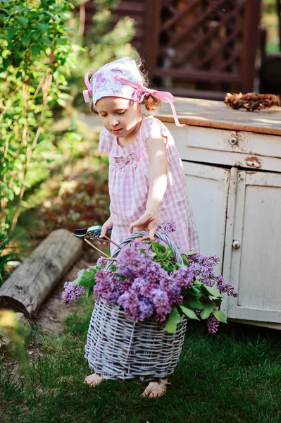 Menina bonito no jardim da primavera com cesta de lilases perto de bureau de madeira vintage — Fotografia de Stock