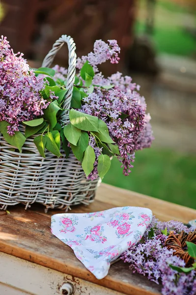 Korg med syrener, blommig pannband och lila krans i vårträdgård — Stockfoto