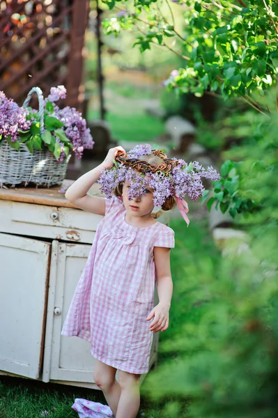 Adorable child girl in lilac wreath in spring garden — Stock Photo, Image