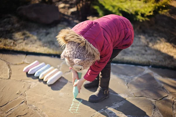 Child girl in pink jacket drawing with chalks in spring garden — Stock Photo, Image