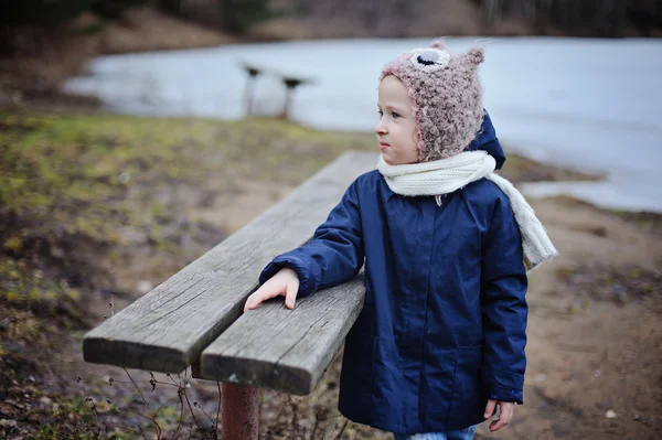 Schattig kind meisje in blauwe vacht en uil hoed op de wandeling op bevroren meer — Stockfoto