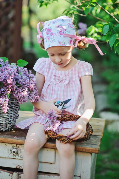 Spring portrait of adorable child girl with basket of lilacs in spring sunny garden — Stock Photo, Image