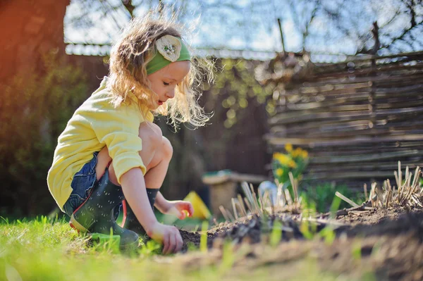 黄色のカーディガンが日当たりの良い早春の庭に花を植えることでかわいい子女の子 — ストック写真