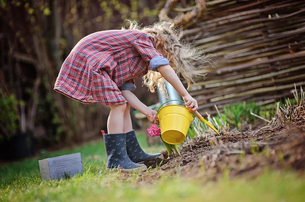 Child girl in plaid dress plays little gardener in spring garden — Stock Photo, Image