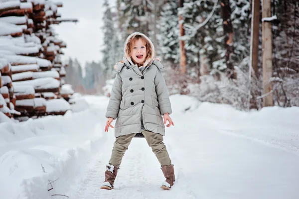 Child girl having fun on the walk in winter snowy forest with tree felling on background