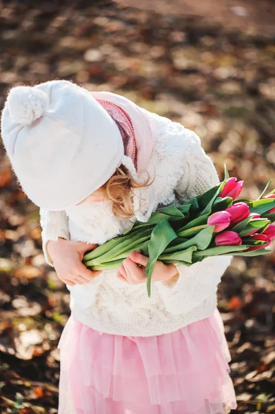 Милая девочка с букетом тюльпанов на женский день на прогулке весной — стоковое фото