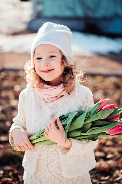 Весенний портрет счастливой улыбающейся девочки с букетом тюльпанов на прогулке в солнечный день — стоковое фото