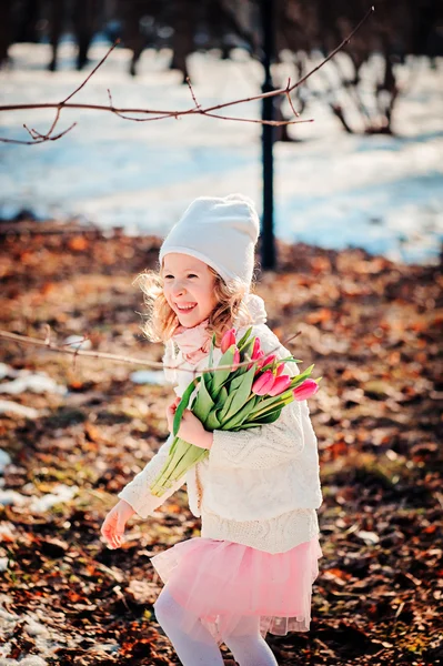 Весняний портрет щасливої усміхненої дівчинки з букетом тюльпанів на прогулянці в сонячний день — стокове фото