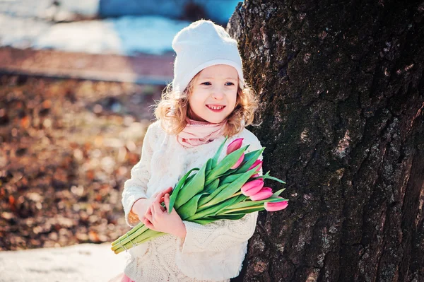 Spring portrait of happy smiling child girl with tulips bouquet on the walk in sunny day — Stock Photo, Image