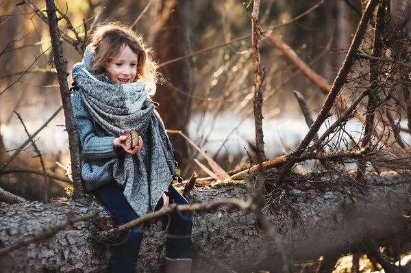 Gelukkig kind meisje zitten en spelen op oude pijnboom in vroege voorjaar bos — Stockfoto