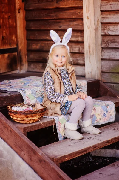 Šťastné dítě dívka, která nosí uši na Velikonoce v dřevěné chatě — Stock fotografie