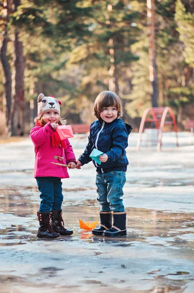 Bambino ragazzo e ragazza divertirsi e giocare barche di carta in pozzanghera primavera — Foto Stock