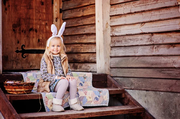 Lyckligt barnflickan bär bunny öron till påsk på trä country house — Stockfoto