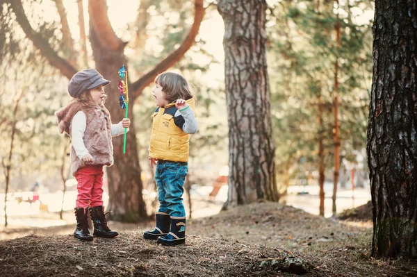 Toddler friends are happy playing whirligig in sunny forest — Stock Photo, Image