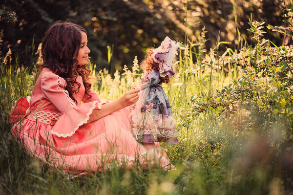 Dreamy kid girl dressed as fairytale princess playing with her doll in summer forest