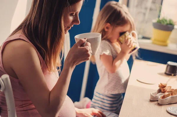 Feliz amor mãe grávida e filha da criança tomando café da manhã e bebendo chá em casa — Fotografia de Stock