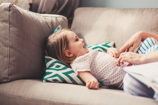 Feliz mãe amorosa e filha da criança se divertindo e fazendo cócegas uns aos outros em casa no sofá — Fotografia de Stock