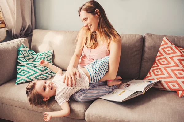 Feliz mãe amorosa e filha da criança se divertindo e fazendo cócegas uns aos outros em casa no sofá — Fotografia de Stock