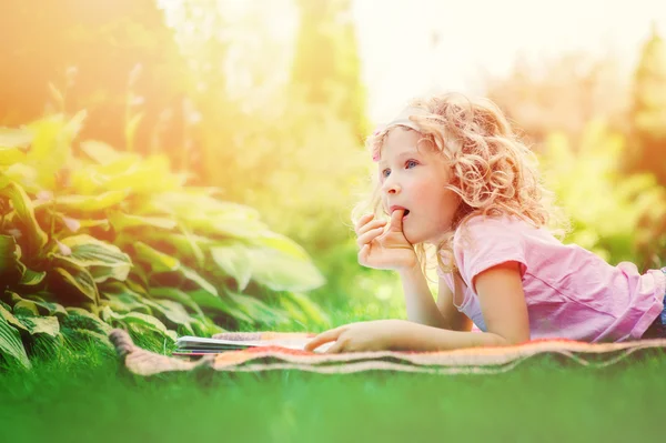 Cute dreamy 6 years old child girl reading book in sunny summer garden — Stock Photo, Image
