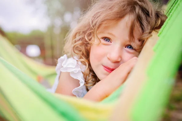 Adorable happy child girl relaxing in colorful hammock in sunny summer garden — Stock Photo, Image