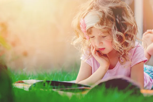 Carino sognante bambino ragazza lettura libro nel soleggiato giardino estivo — Foto Stock
