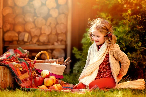 Lyckligt barn flicka i vit stickad halsduk med röda äpplen i soliga höst trädgård — Stockfoto