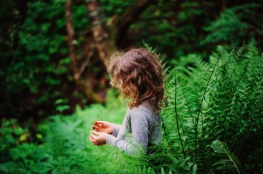 child girl in summer forest exploring nature, learning on vacation