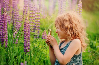 child girl exploring nature with loupe, learning on summer vacation in forest