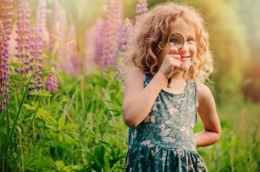 child girl exploring nature with loupe, learning on summer vacation in forest