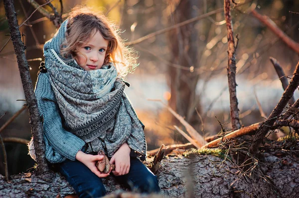 Child girl sitting on pine tree on cozy warm outdoor winter walk in snowy forest — Zdjęcie stockowe