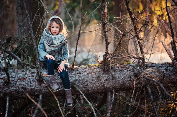 Child girl sitting on pine tree on cozy warm outdoor winter walk in snowy forest — Stok fotoğraf