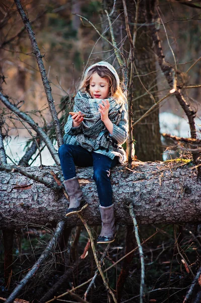 Child girl sitting on pine tree on cozy warm outdoor winter walk in snowy forest — Stock Photo, Image