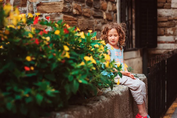 儿童女孩坐在石头墙和气味的花朵 — 图库照片