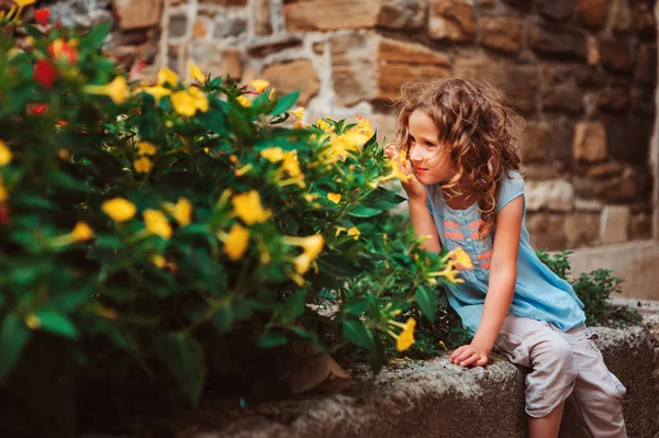 Bambino ragazza seduta su muro di pietra e fiori odore — Foto Stock