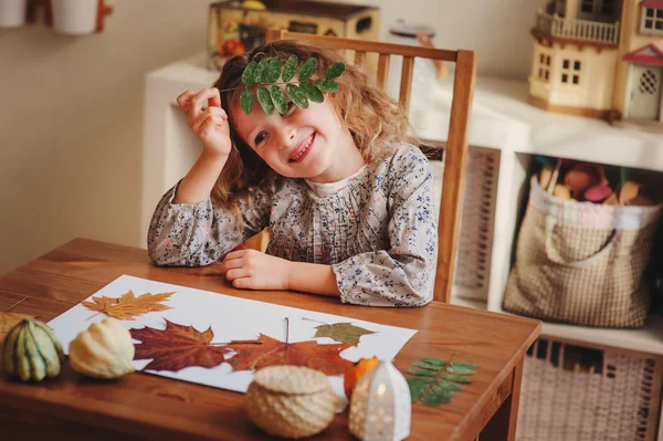 Niña feliz haciendo hojas secas herbario en casa, ambiente acogedor otoño — Foto de Stock