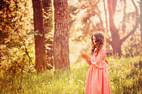 Curly child girl dressed as fairytale princess playing with dandelions in summer forest