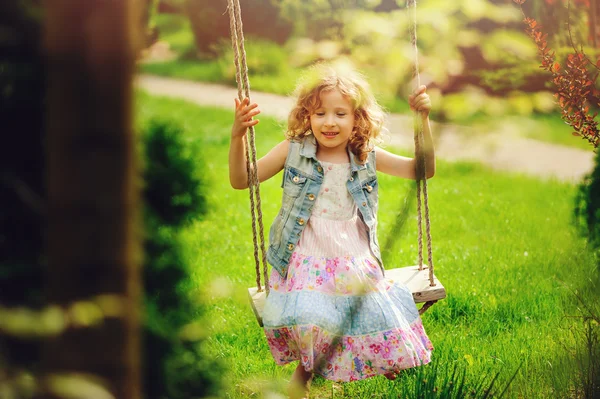 Happy child girl relaxing on swing in spring garden, spring vacation outdoor activities — Stock Photo, Image