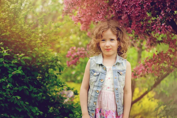 Cute child girl in jeans vest enjoying spring near blooming crab apple tree in country garden — Stock Photo, Image