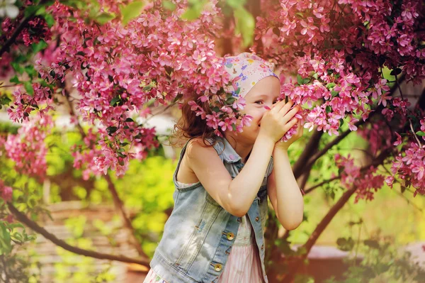 Bonito criança menina no jeans colete aproveitando primavera perto florescendo caranguejo maçã árvore no país jardim — Fotografia de Stock