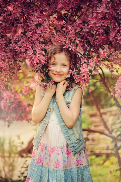 Niedliche Kind Mädchen in Jeans Weste genießen den Frühling in der Nähe blühenden Krabben Apfelbaum im Garten — Stockfoto