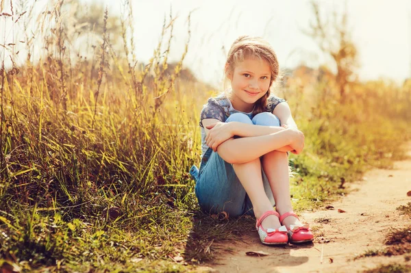 Szczęśliwy dziecko dziewczyna w dżinsach ogólnie gra na słonecznym polu, lato outdoor styl życia, przytulny nastrój — Zdjęcie stockowe