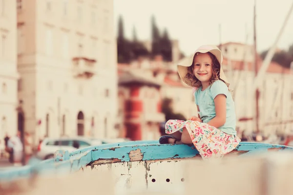 Niña feliz sentada en barco viejo en vacaciones de verano en Piran, Eslovenia, con vista de la ciudad en el fondo — Foto de Stock