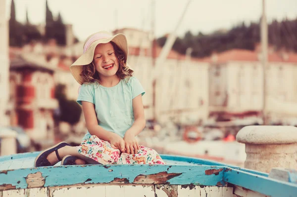 Szczęśliwe dziecko dziewczynka siedzi w starej łodzi na wakacje w Piran, Słowenia, z widokiem na miasto na tle — Zdjęcie stockowe
